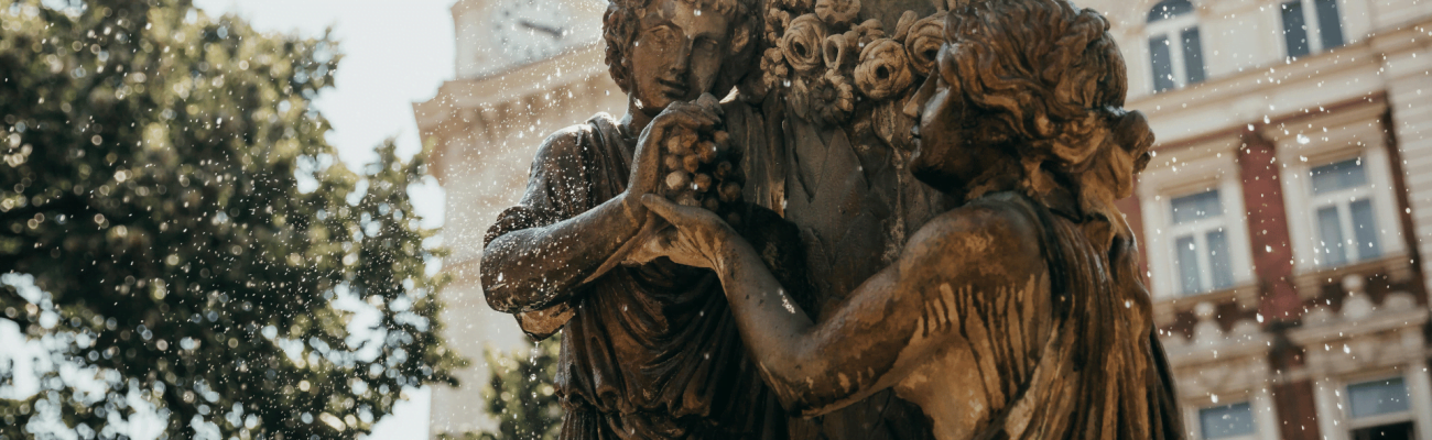 Two women are depicted in a statue, holding hands together in front of a grand building, representing solidarity and connection.