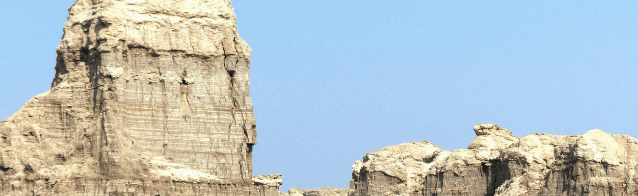 A large, rugged rock formation stands isolated amidst the endless sands of a sunlit desert.